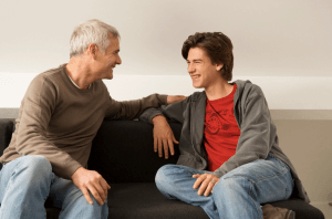 Two men sitting on a couch talking to each other.