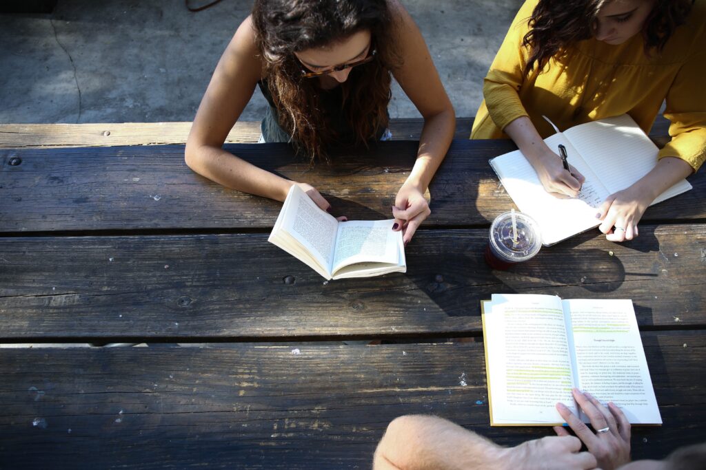 3 people sitting at a wood table studying