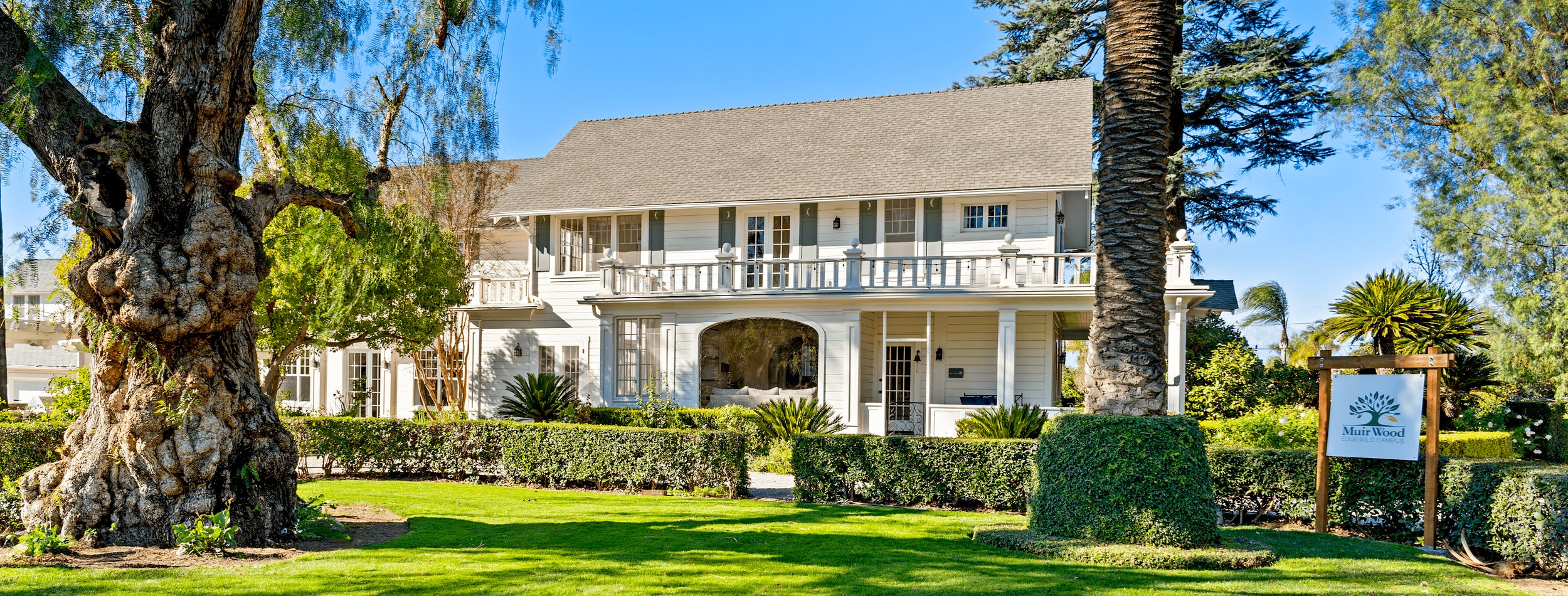 The exterior of a Muir Wood treatment center. The white home has two levels and large trees in the front yard.