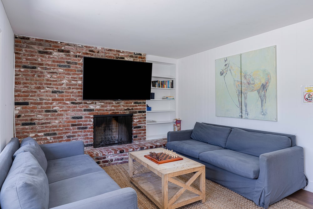 Living room with two blue couches around a coffee table, a fireplace and wall mount tv on the opposite wall.