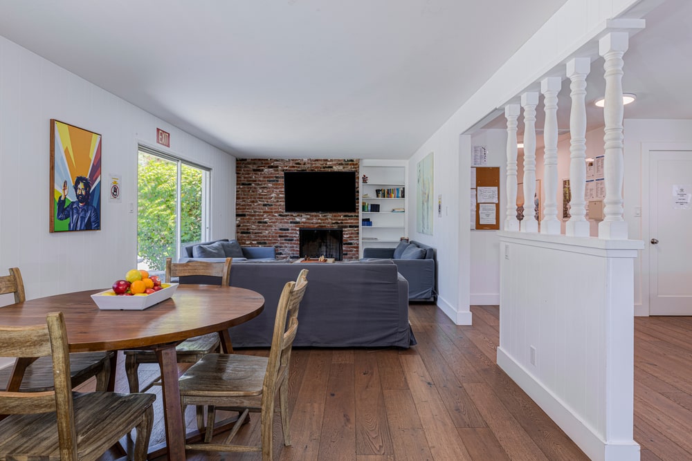 A living room and dining area with a wooden table, three blue couches around a coffee table, fireplace, and wall-mounted TV.