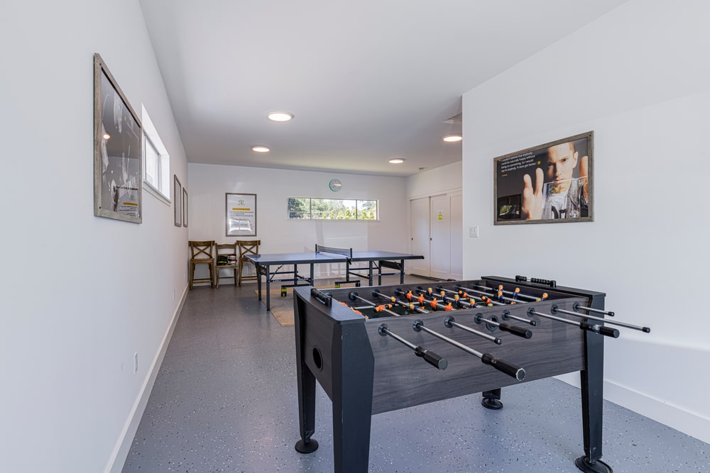 A room with a foosball table, ping pong table and chairs against the wall.