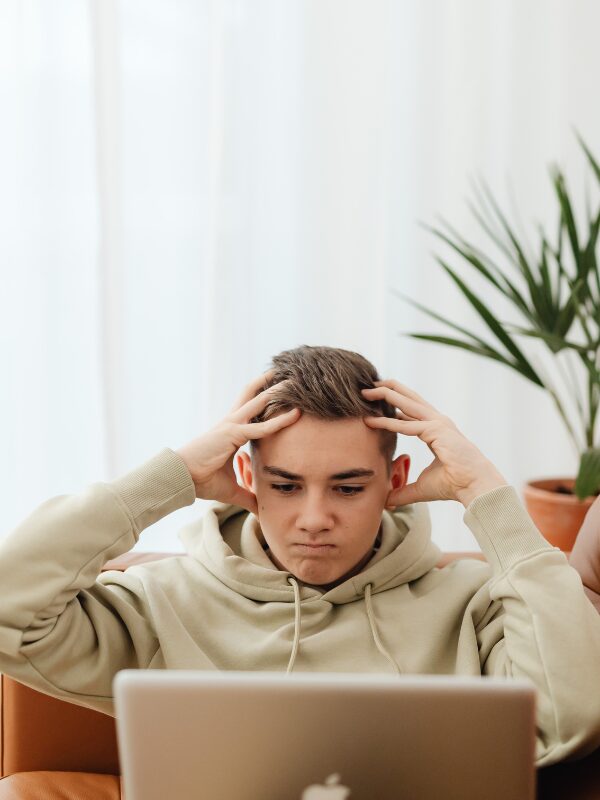 a teen sitting with their laptop holding their head in their hands