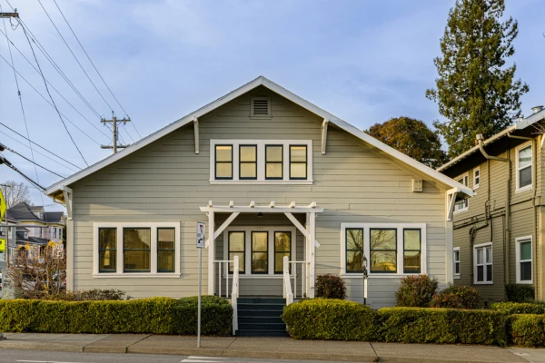 A front view of a tan two-story residential treatment facility for boys with green window trim and manicured bushes.