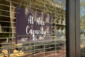 A purple sign hanging in a window reads "At Max Capacity," indicating high demand for treatment services.